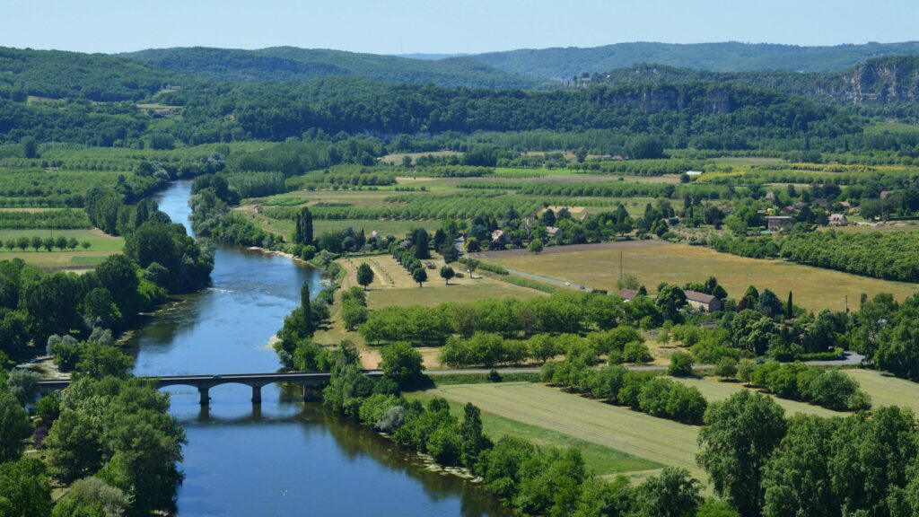 A scenic view of the Dordogne River flowing through the lush French countryside in summer.