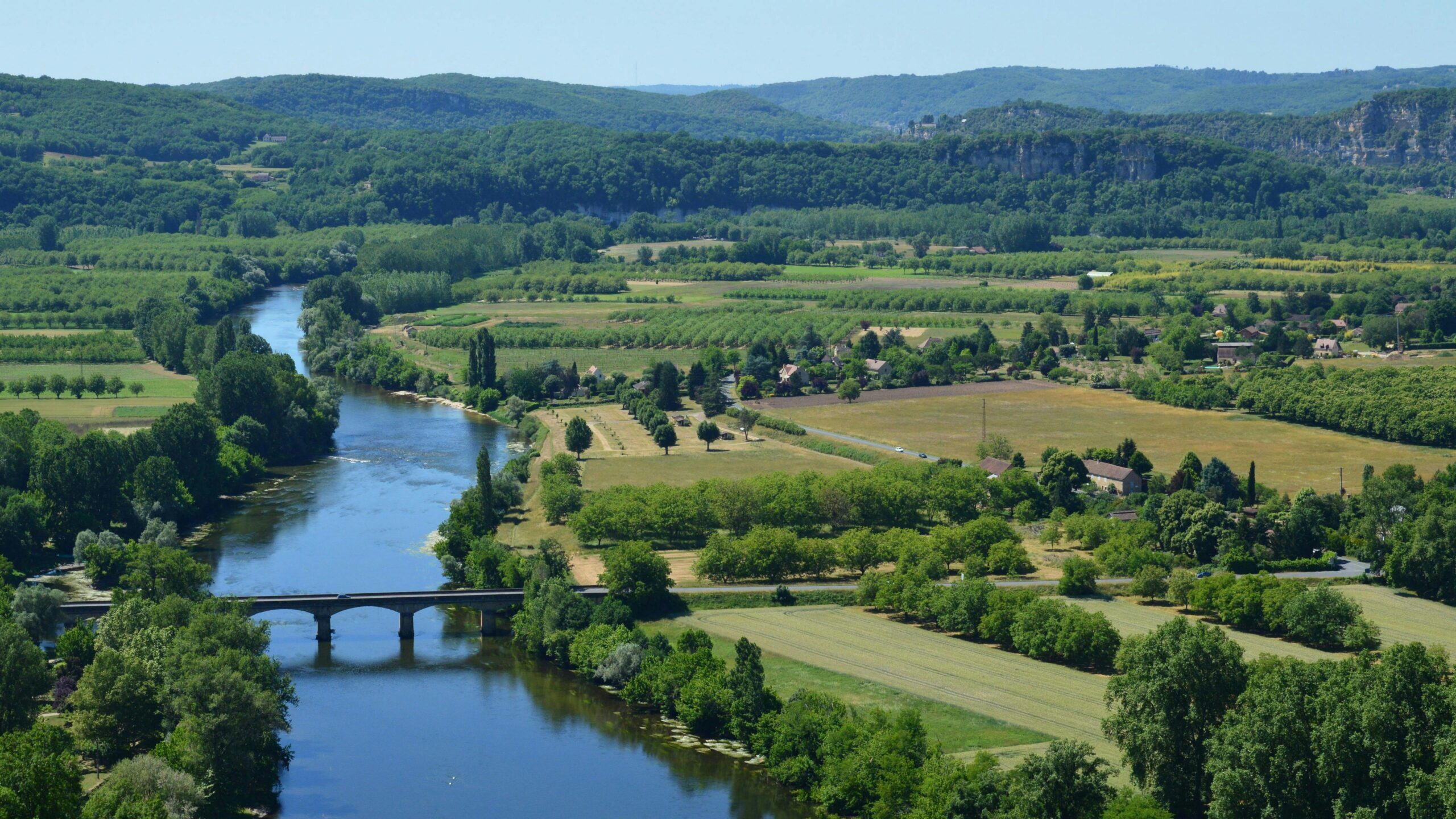 A scenic view of the Dordogne River flowing through the lush French countryside in summer.
